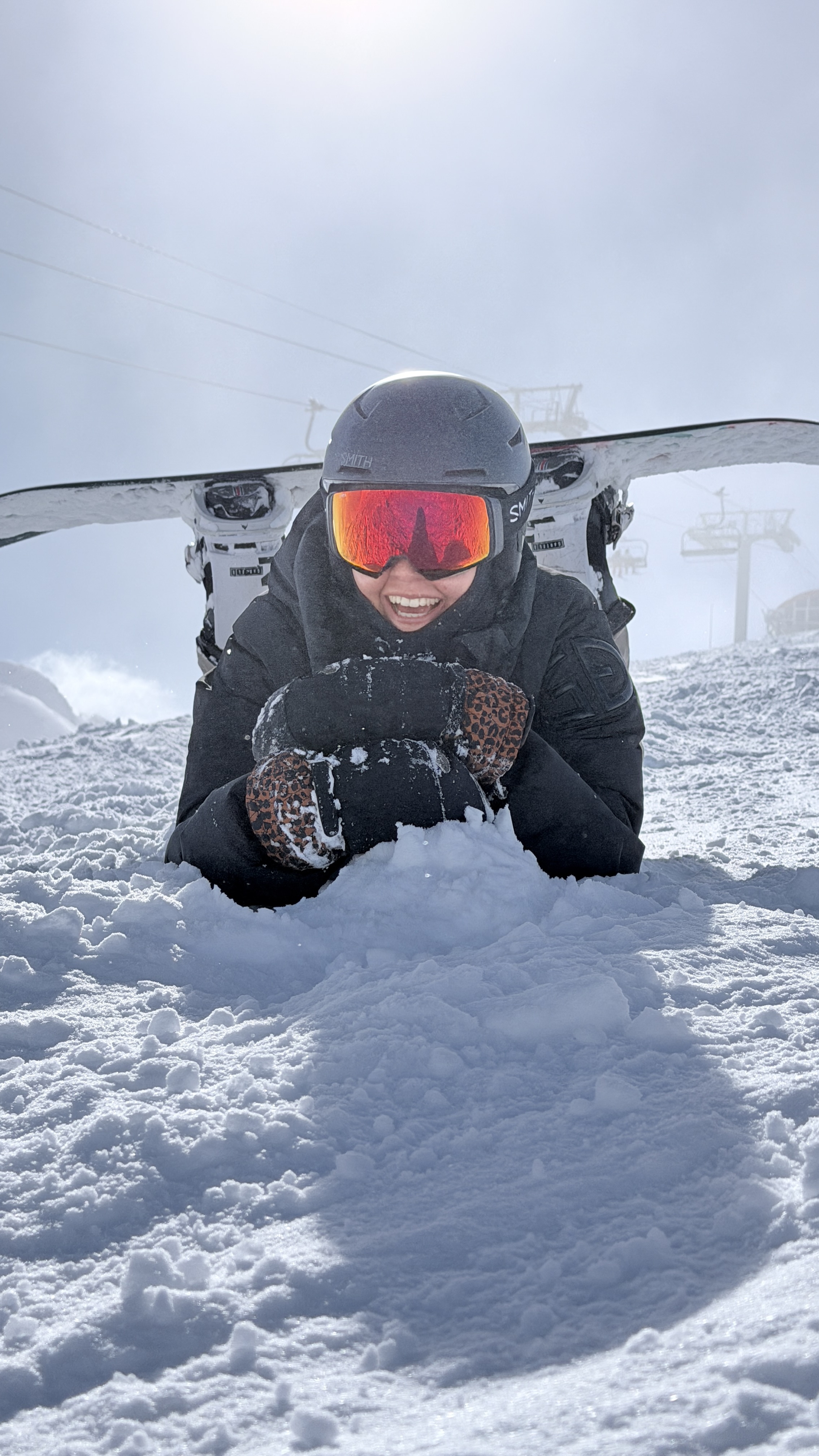 Laughing snowboarder lying in the snow with red goggles and leopard mittens