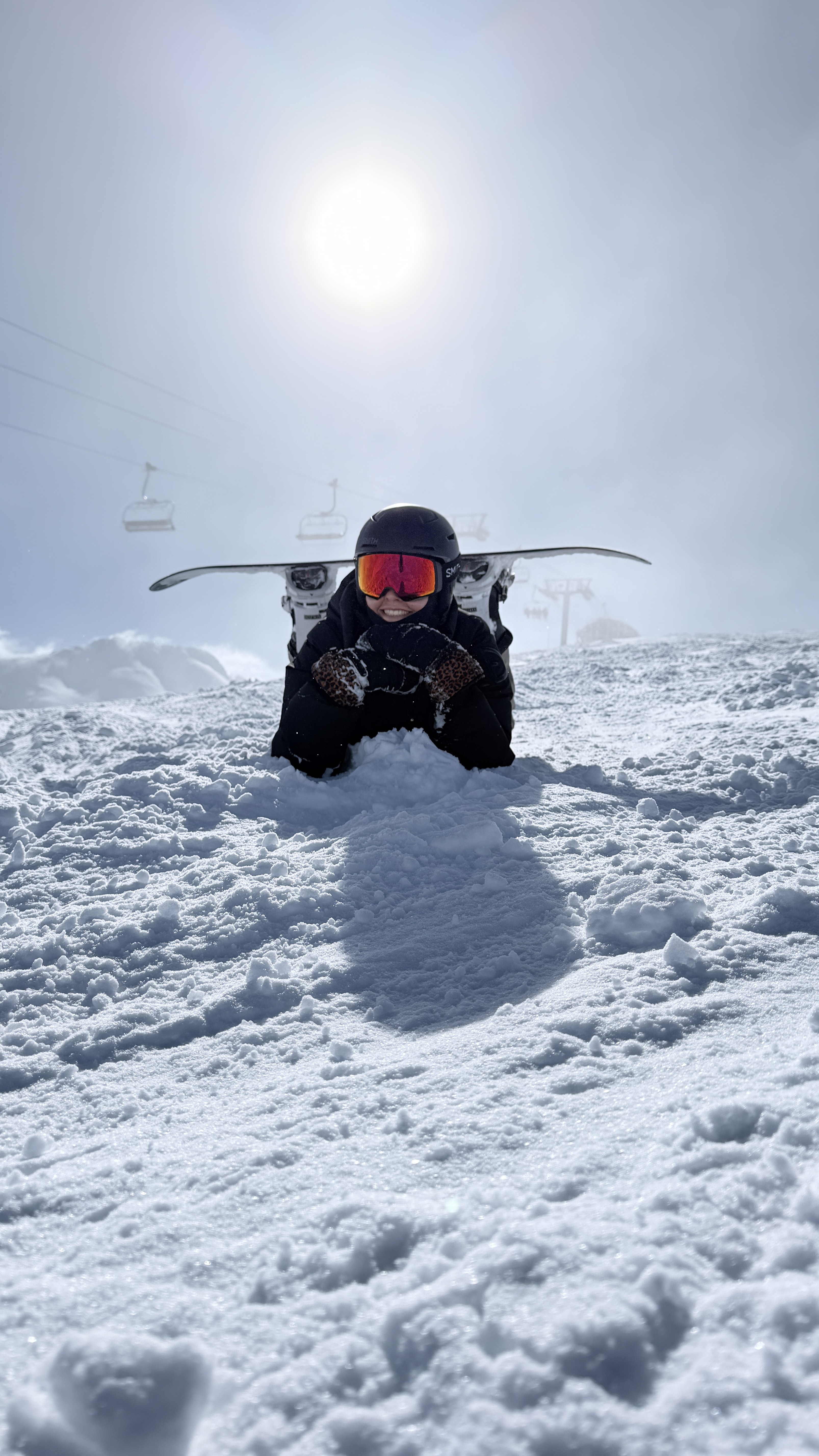 Snowboarder lying in the snow under a hazy sun with a chairlift in the background