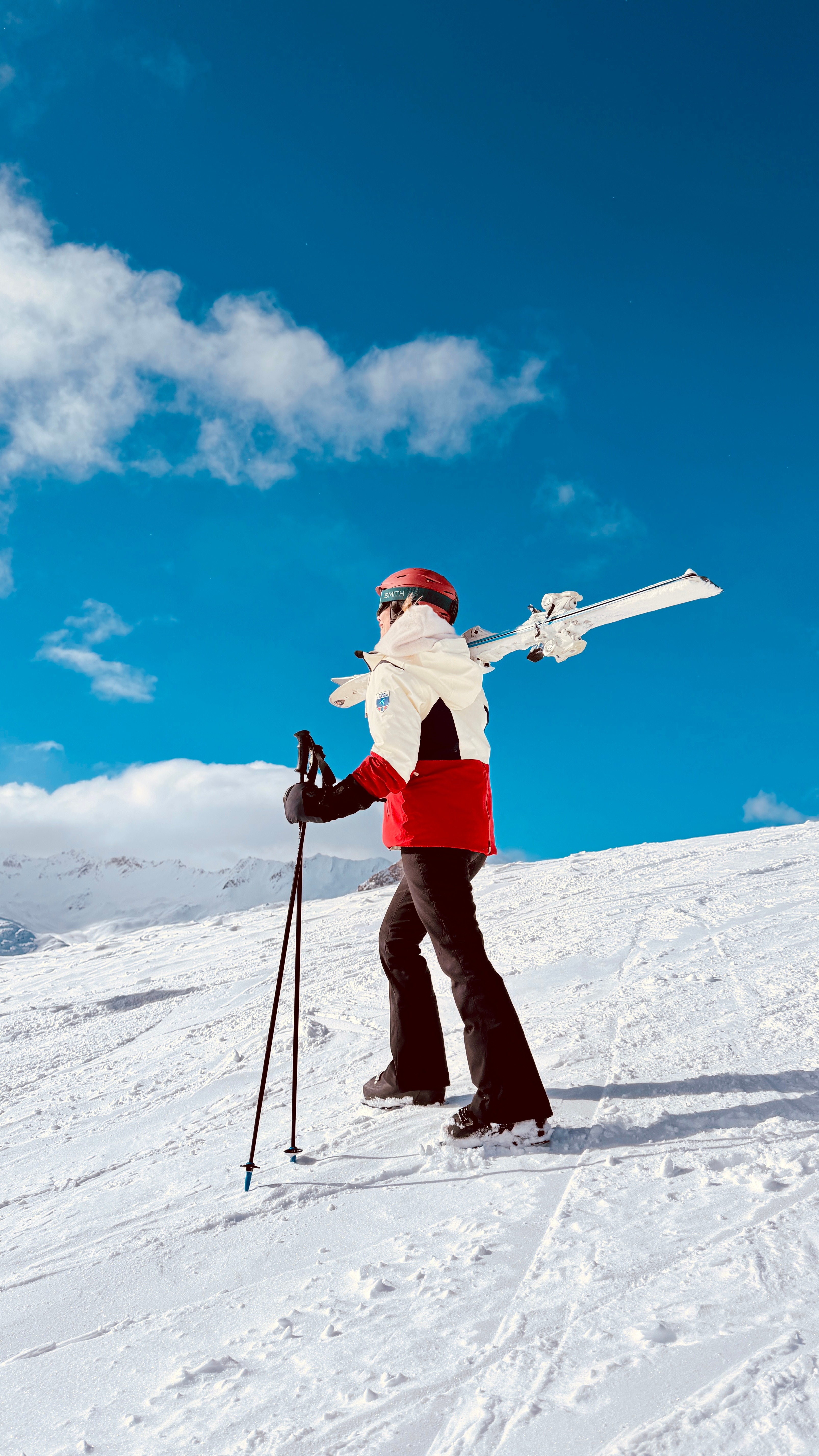 Skier walking up the slope with her skis on her shoulder under a deep blue sky