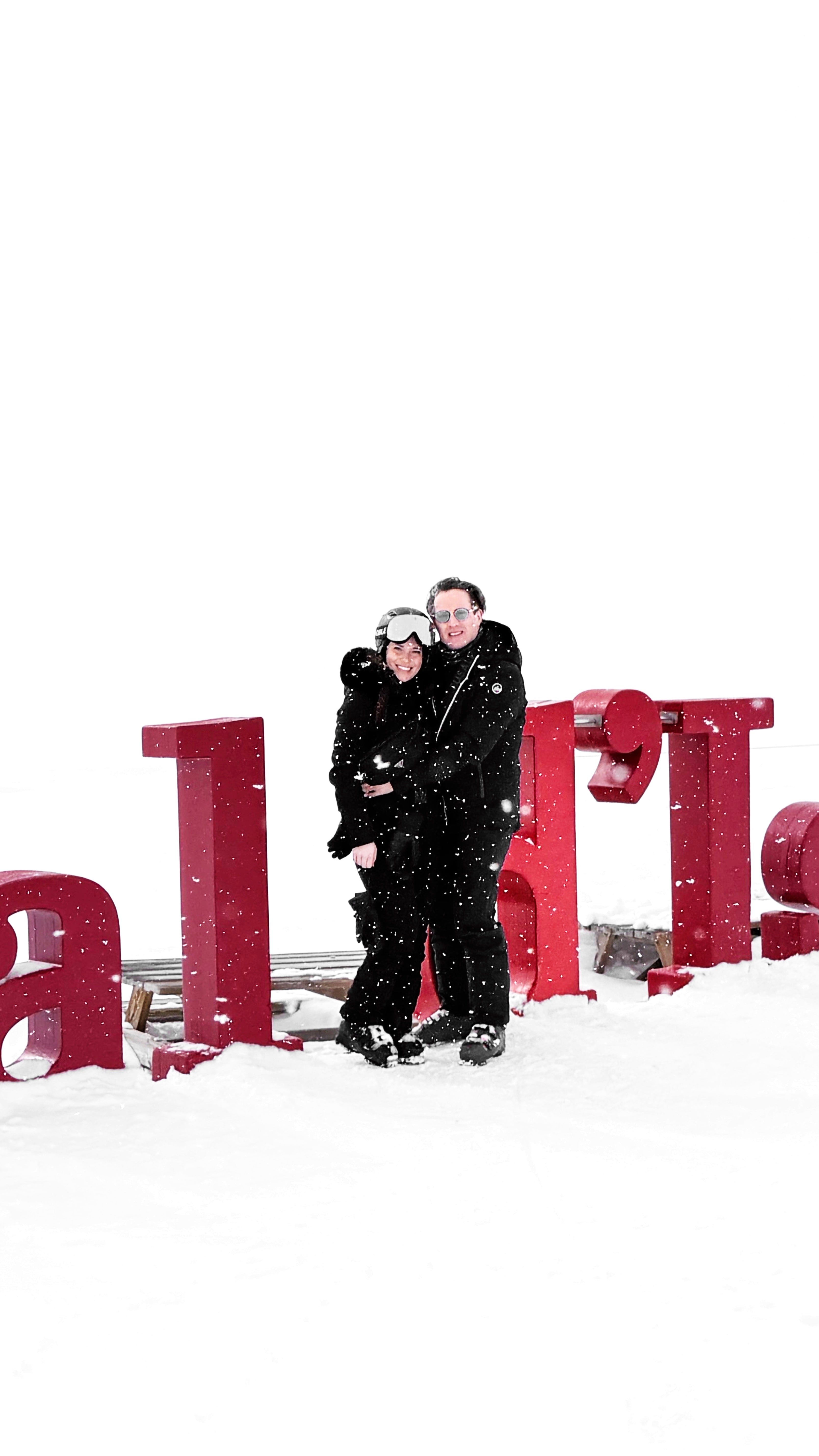 Couple embracing under falling snow in front of the Val d'Isère letters