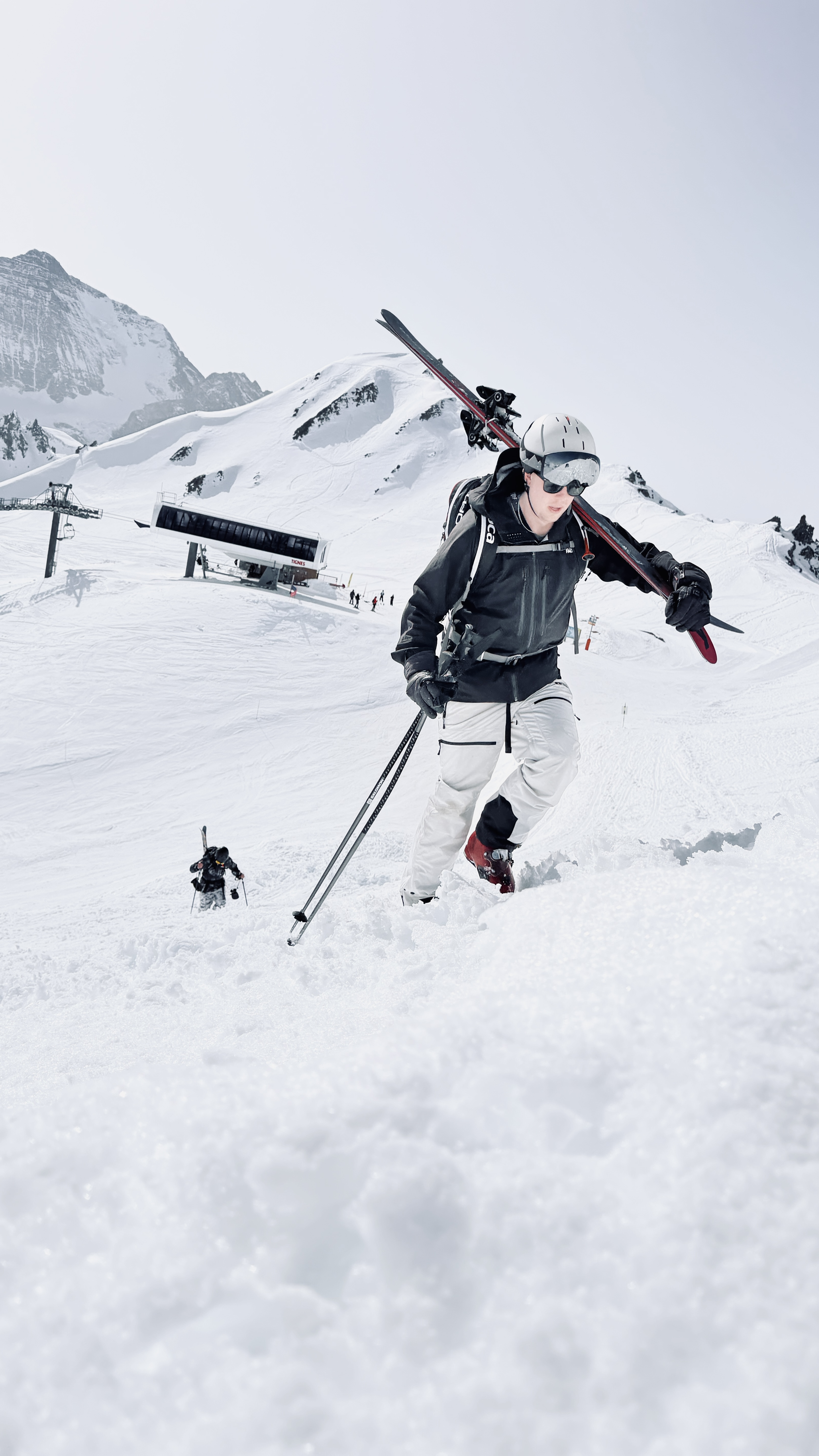 Freerider bootpacking up a snowy ridge with skis on his shoulder above a Tignes chairlift