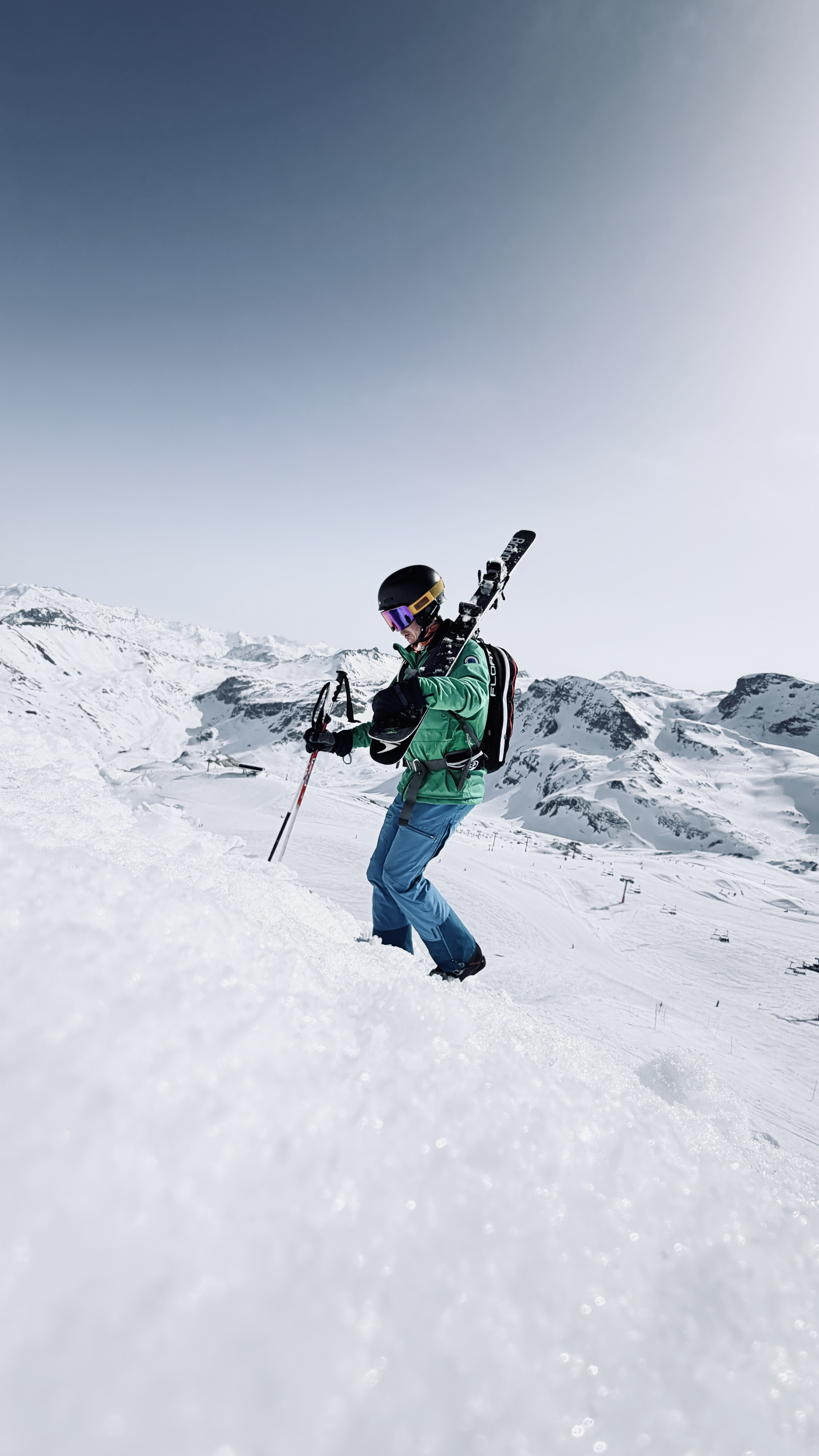 Skier in a green jacket climbing a snowy ridge with skis on his backpack