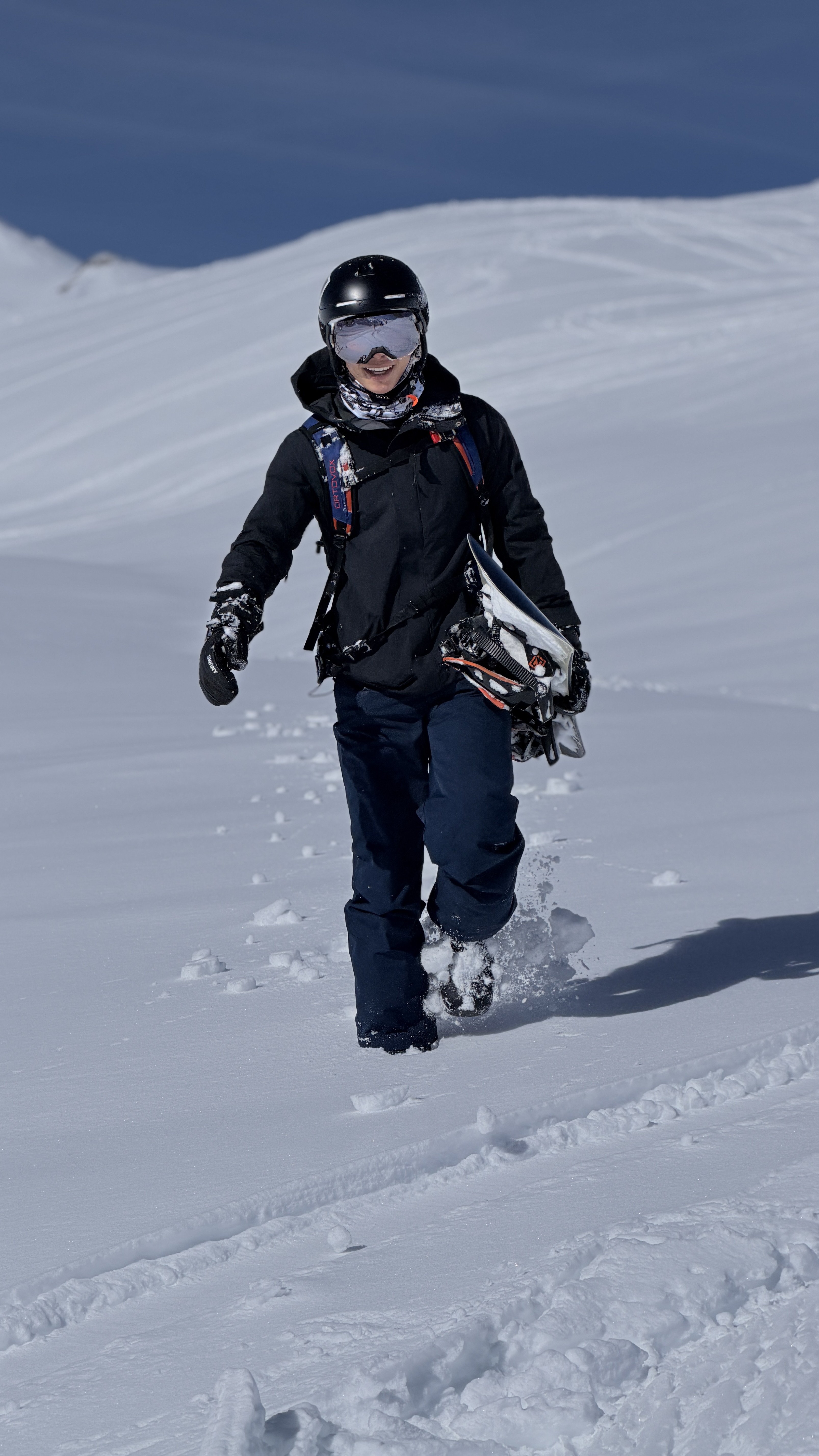 Smiling snowboarder walking through fresh powder with his board under his arm